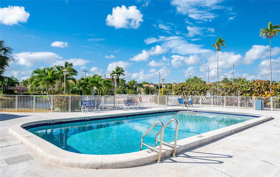 Outdoor swimming pool with a surrounding fence and lounge chairs.