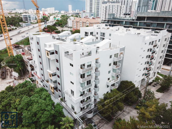 Aerial view of a multi-story residential building complex in an urban area with high-rise structures in the background.