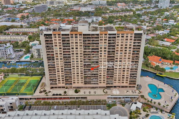 Aerial view of a high-rise residential building with balconies, surrounded by various other buildings and amenities.