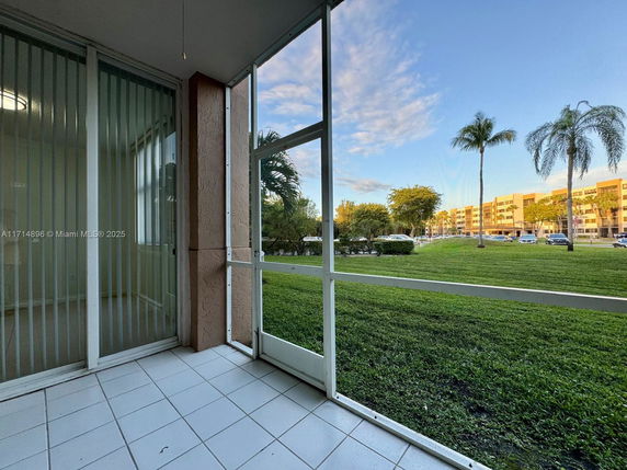 View of a grassy outdoor area with palm trees and residential buildings in the background.