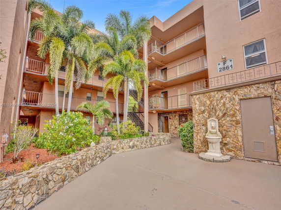 Front view of a multi-story residential building with balconies and a stone wall facade.