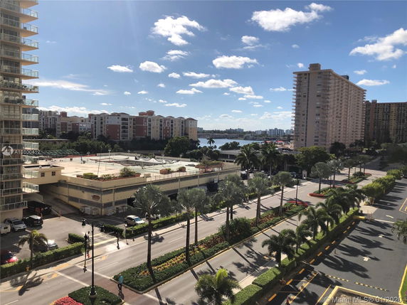 View of multiple apartment buildings with a road and palm trees in the foreground.