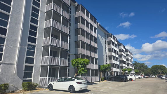 Front view of a multi-story apartment building with balconies and a parking area.