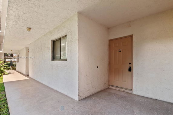 Exterior walkway leading to a beige door with a small window beside it.