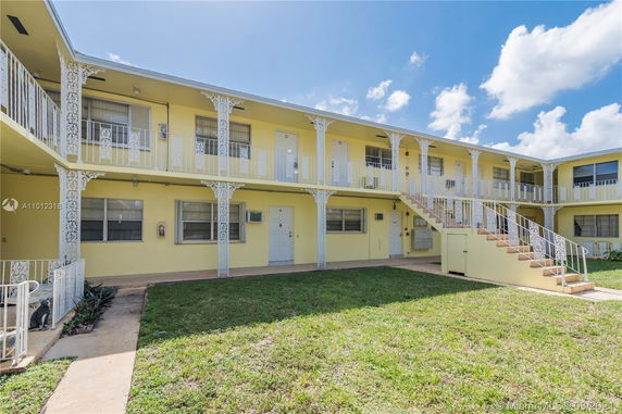 Front view of a two-story yellow apartment building with decorative railings and external staircases.
