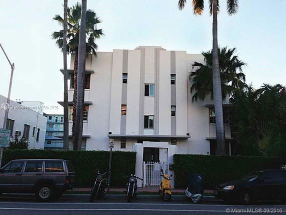 Front view of a multi-story building with palm trees and a gated entrance.