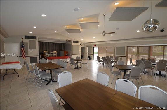 Interior view of a club house with tables and chairs, stage, and ceiling lights.