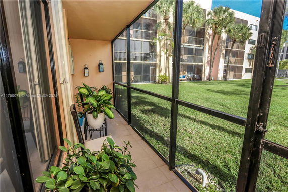 View from a screened patio overlooking a grassy area and an apartment building with balconies.