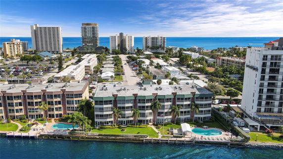 View over a waterfront residential complex with multiple multi-story buildings and a pool, overlooking the ocean.