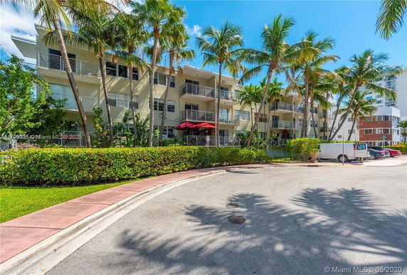 Front view of a multi-story apartment building with balconies and tropical landscaping.