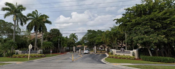 Entrance view of Palm Aire Gardens with a gated access and surrounding greenery.