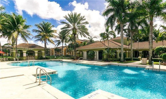 Outdoor swimming pool area with palm trees and surrounding buildings.