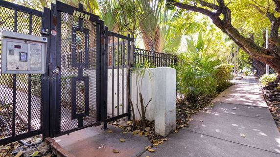 Iron gate with keypad entry adjacent to a sidewalk and trees.