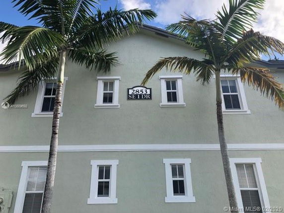 Front view of a two-story house with light green exterior and palm trees.