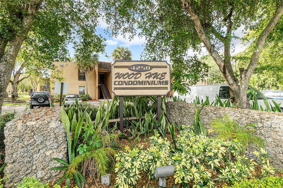 Front view of a condominium building with an entrance sign and surrounding greenery.
