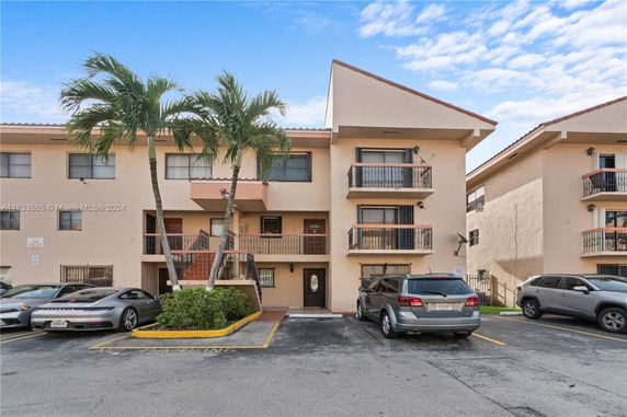 Front view of a multi-story residential building with balconies and parking spaces in front.