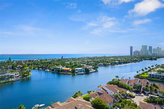 Panoramic view of residential area by a large body of water with distant city skyline.