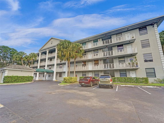 Front view of a four-story apartment building with balconies and parking area.