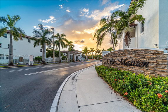 Street view with palm trees and a brick sign marked 'St Maarten' beside a white building.