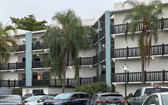 Front view of a multi-story residential building with balconies and palm trees.