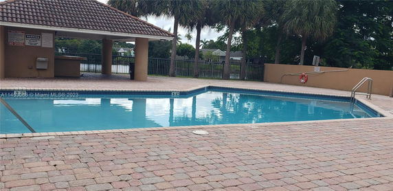Outdoor swimming pool area with tiled deck and a small shaded structure.