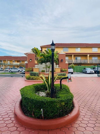 Front view of a multi-story residential building with a gated entrance and landscaped area.