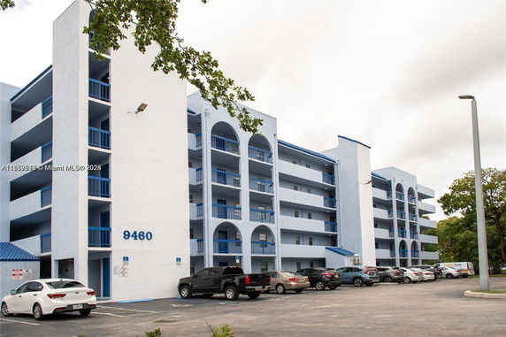 Front view of a multi-story building with balconies and parking area.