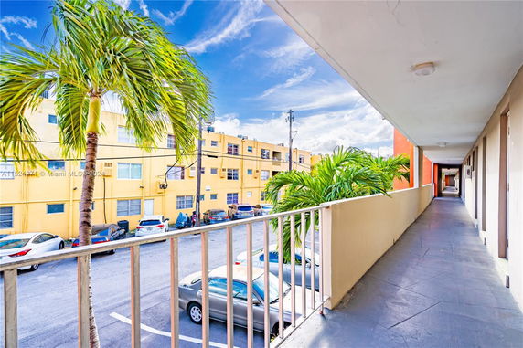 View from a walkway overlooking parked cars and a yellow apartment building.