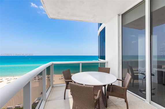 Balcony with a round table and chairs overlooking the ocean and beach.