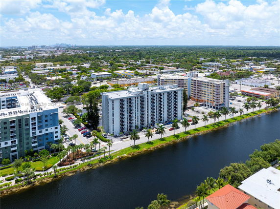 Aerial view of a multi-story residential building alongside a canal with surrounding cityscape.