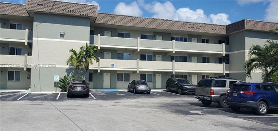 Front view of a three-story apartment building with a parking area in front.
