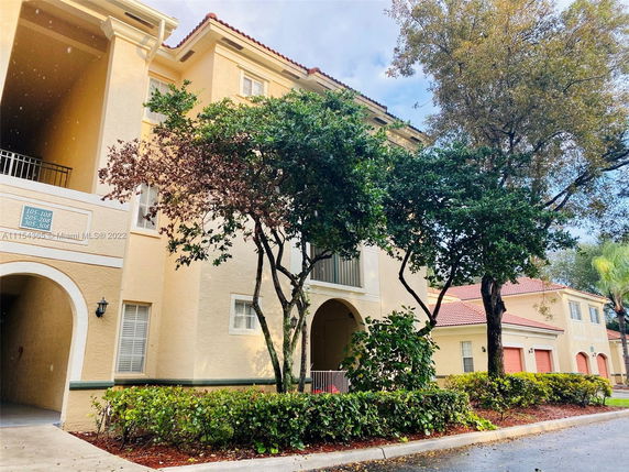 Front view of a multi-story apartment building with balconies and a garden area.