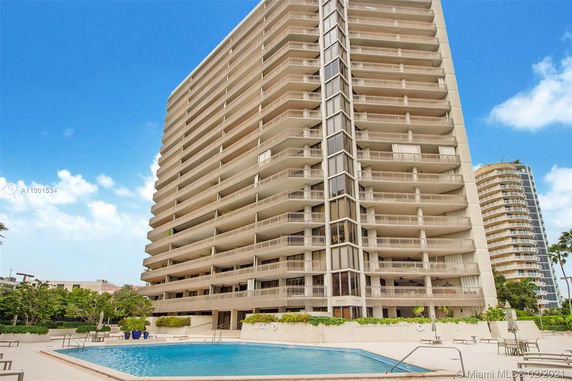 Front view of a high-rise residential building with multiple balconies and a pool area.
