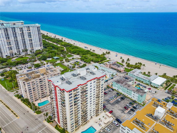 Aerial view of beachfront high-rise apartment buildings with parking areas and nearby ocean beach.