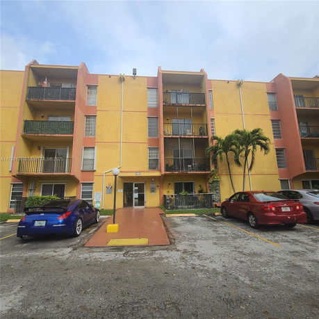Front view of a four-story apartment building with balconies and parking area.