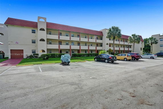 Front view of a multi-story building with open walkways and parking area.