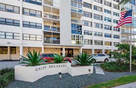 Front view of a multi-story residential building with balconies and a parking area.