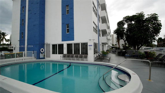 View of a multi-story building with a blue and white exterior, featuring a swimming pool and patio area with seating.