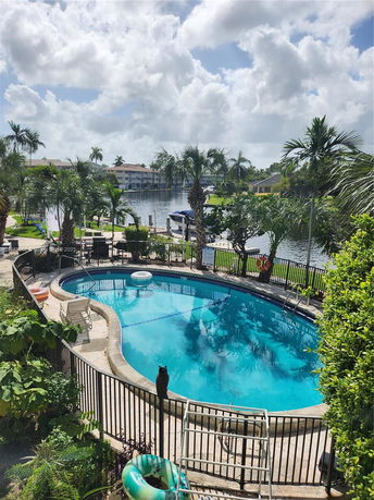 Outdoor swimming pool surrounded by a fence, with chairs and a small garden area nearby.