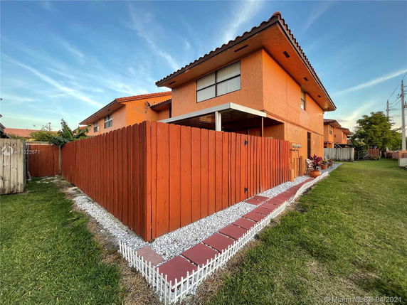 Front view of a two-story house with orange exterior and a fenced yard.