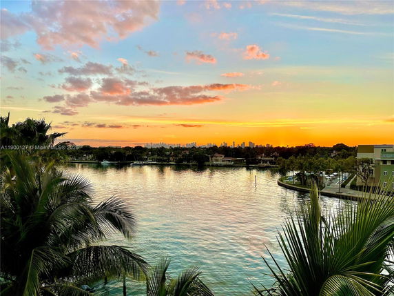 Panoramic view of a waterway with a city skyline in the distance during sunset.