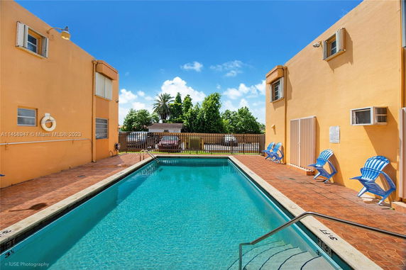 Outdoor swimming pool with surrounding buildings and deck chairs.
