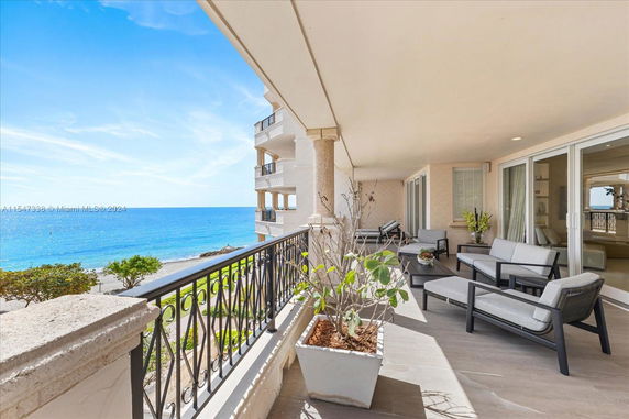 View from a balcony overlooking a beach with comfortable seating and glass sliding doors leading inside.