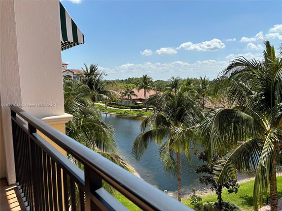 View from a balcony overlooking a lake and palm trees with residential buildings in the background.