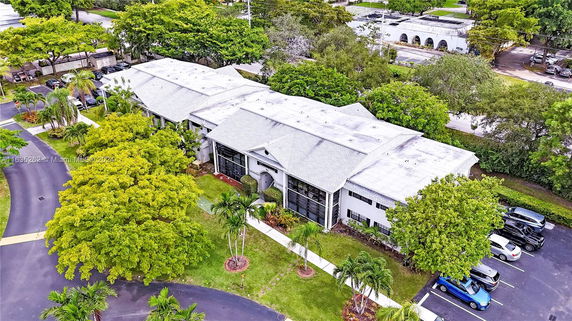 Aerial view of a large building with a white roof, surrounded by trees and a parking area.