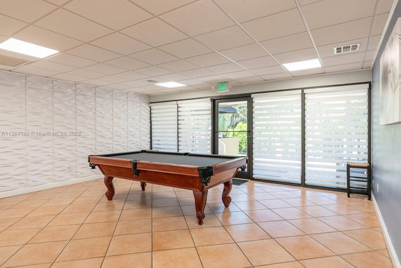 Room with a billiard table and large windows with blinds.