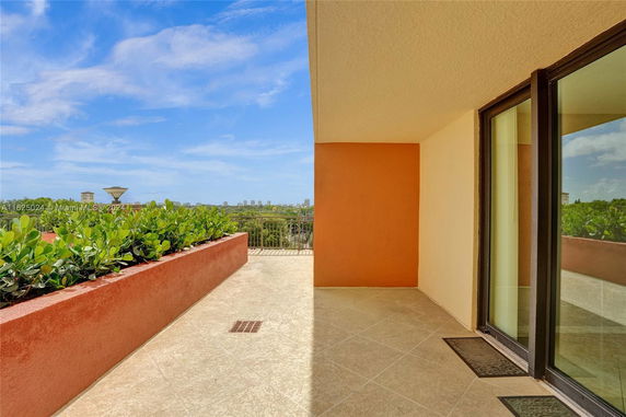 View from a terrace with a partial wall and glass doors overlooking greenery and distant buildings.