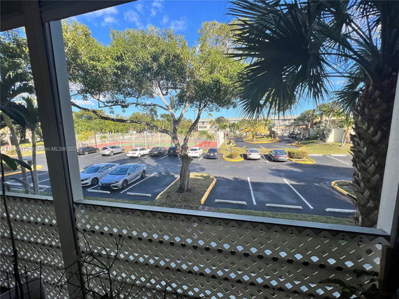View of a parking area with several cars and trees, seen from a building.