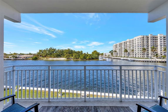 Waterfront view from a balcony overlooking a body of water with buildings and trees in the distance.