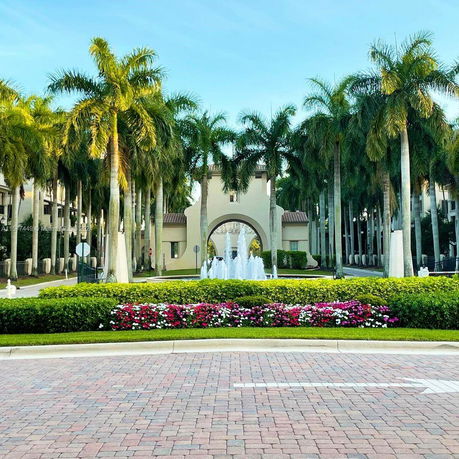 Front view of a building with an arch and fountain, surrounded by palm trees.